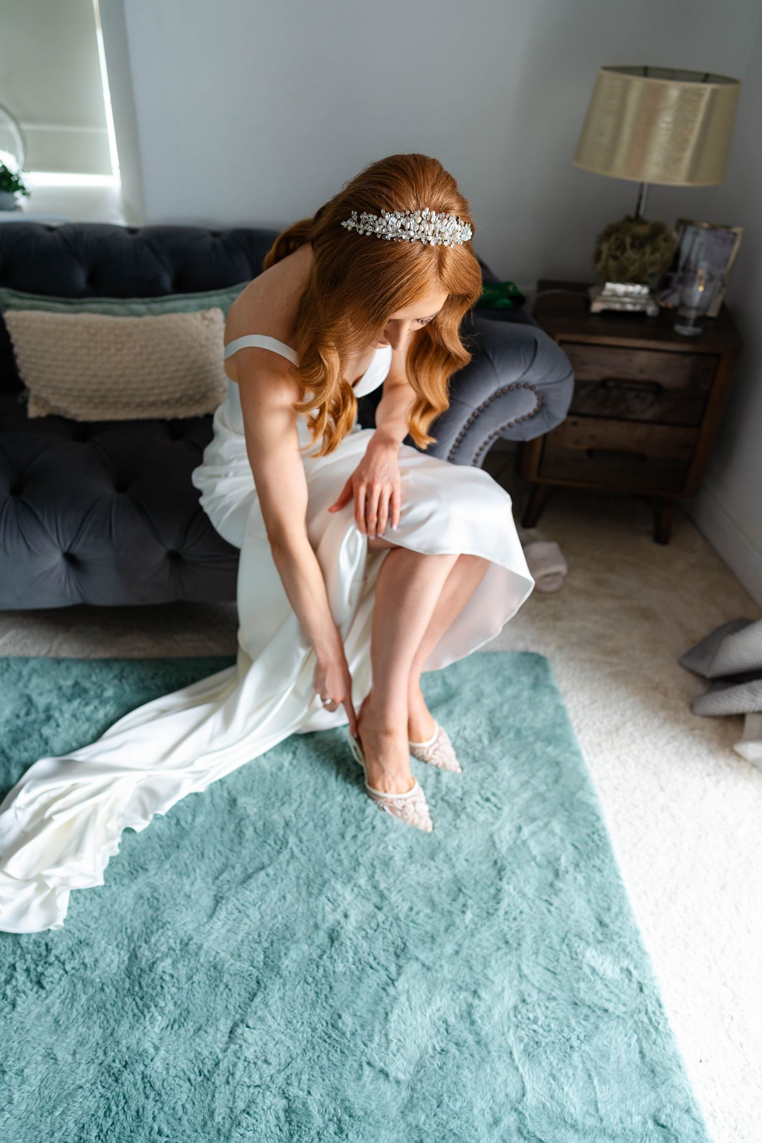 Bride in white dress sits elegantly on a mint green carpet in a sunlit room.
