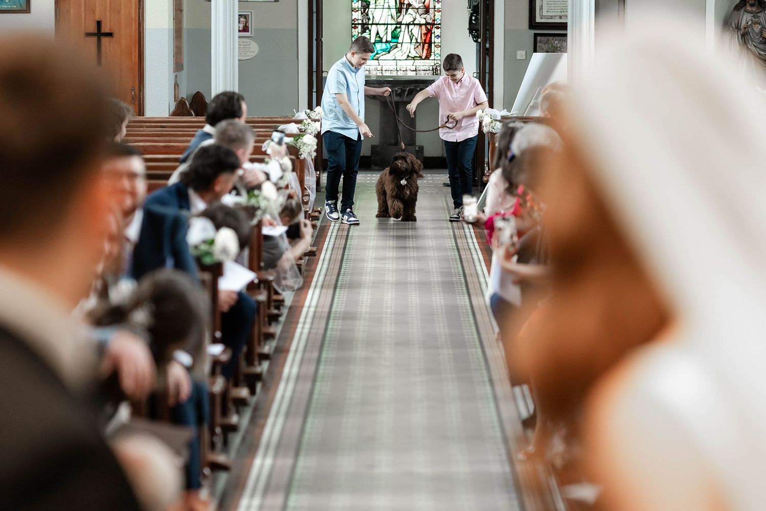 Wedding ceremony guests seated in wooden pews inside an elegant church with stained glass windows.