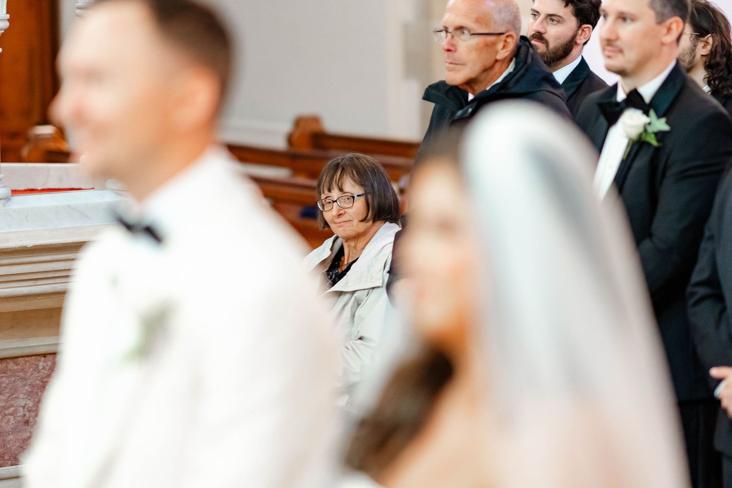 Wedding guests gather in formal attire at an indoor ceremony venue with elegant decor and lighting.