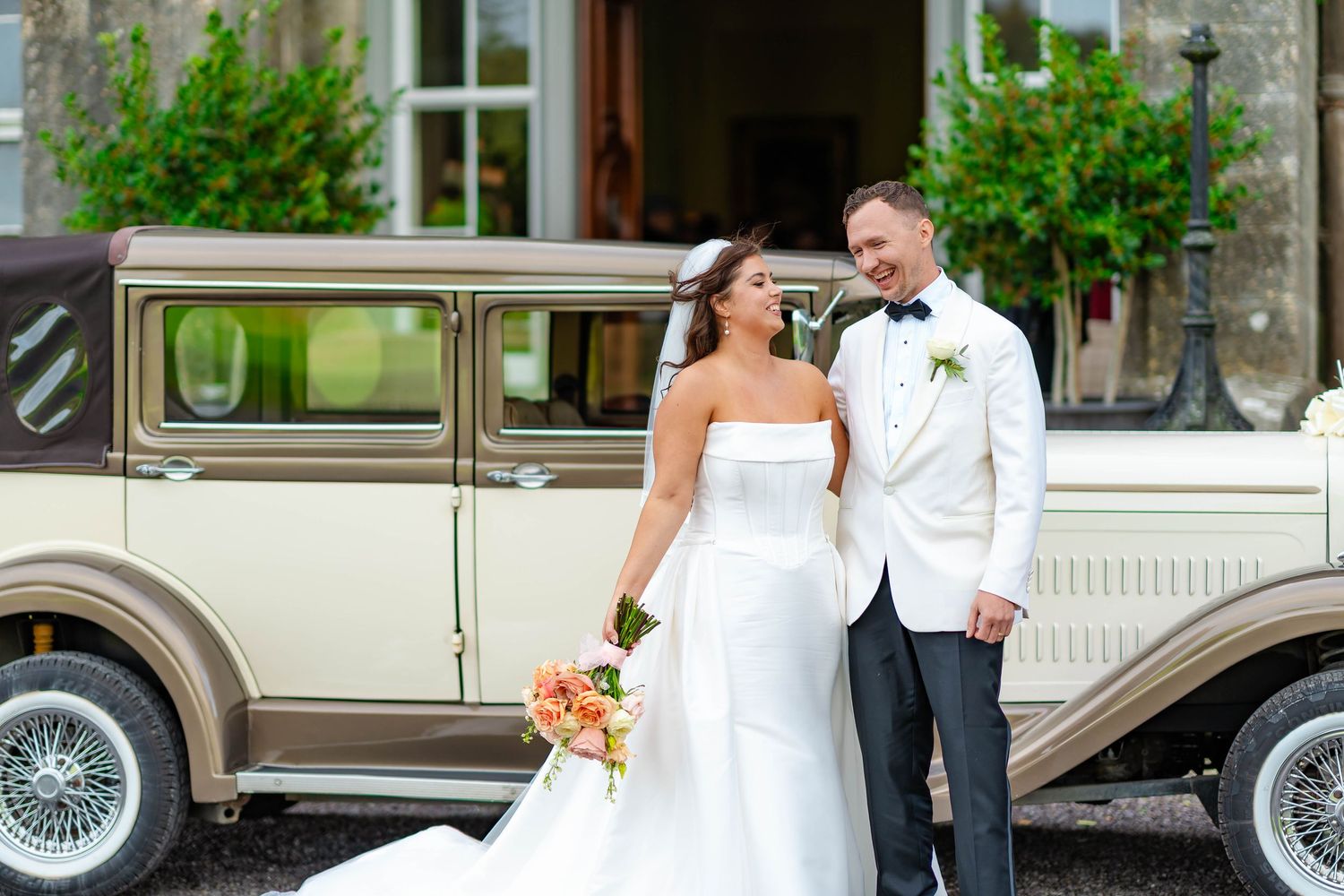 Wedding couple shares an intimate moment in front of vintage cars during an outdoor celebration.