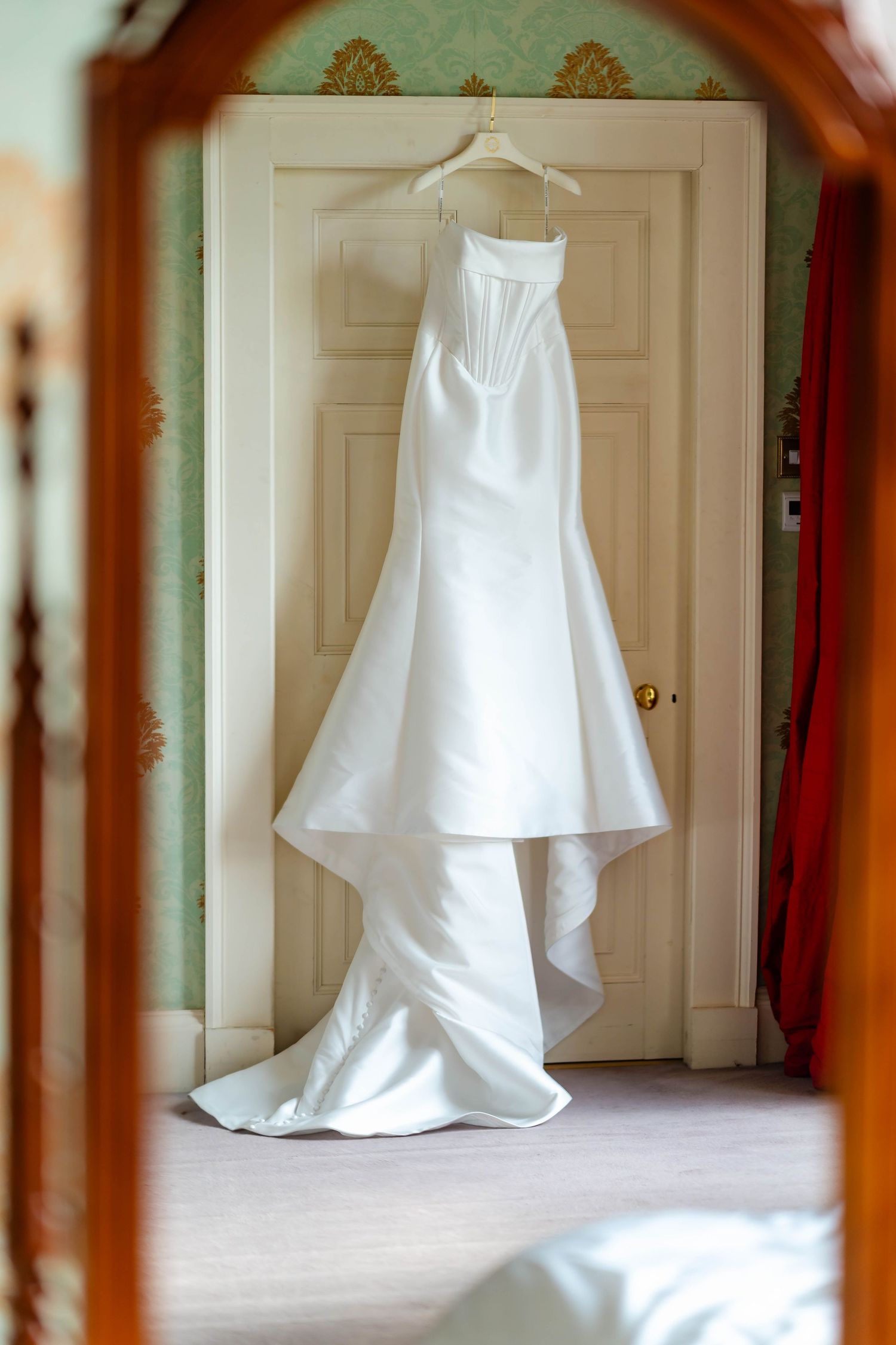White wedding dress displayed hanging in a doorway showing its elegant silhouette and train from multiple angles.