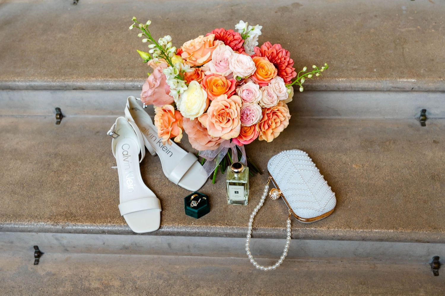 Peach and coral roses arranged in white vases on rustic wooden planks with scattered pearls and decorative elements.