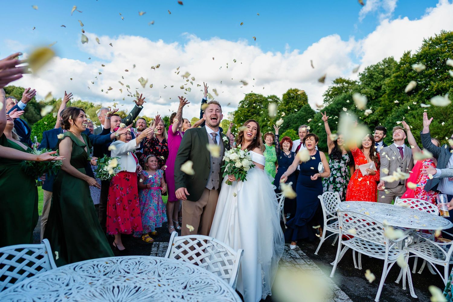 Joyful wedding celebration with guests throwing confetti under bright blue skies.