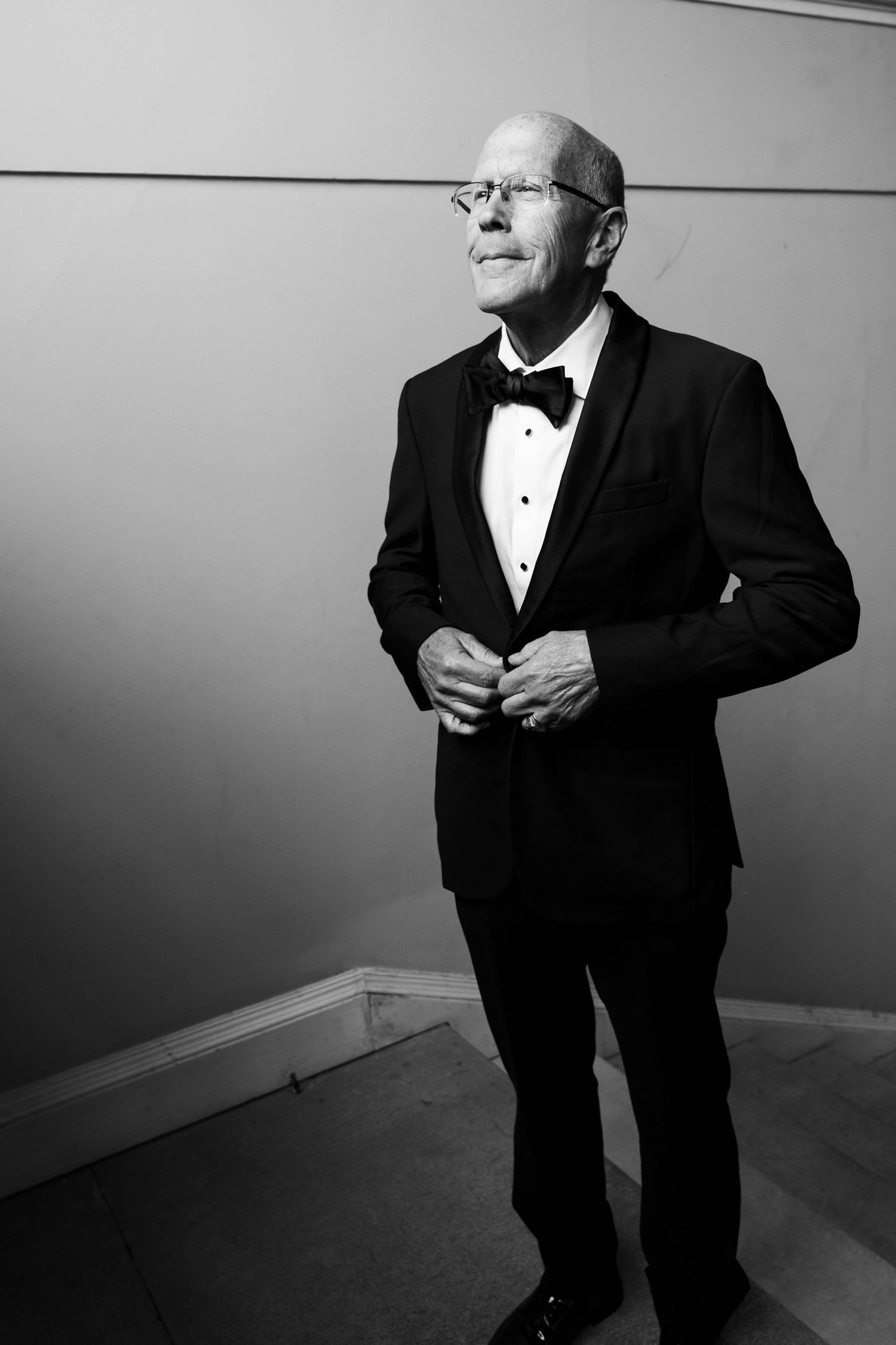 A black and white photo series showing someone in a tuxedo and glasses posing in different expressive positions.