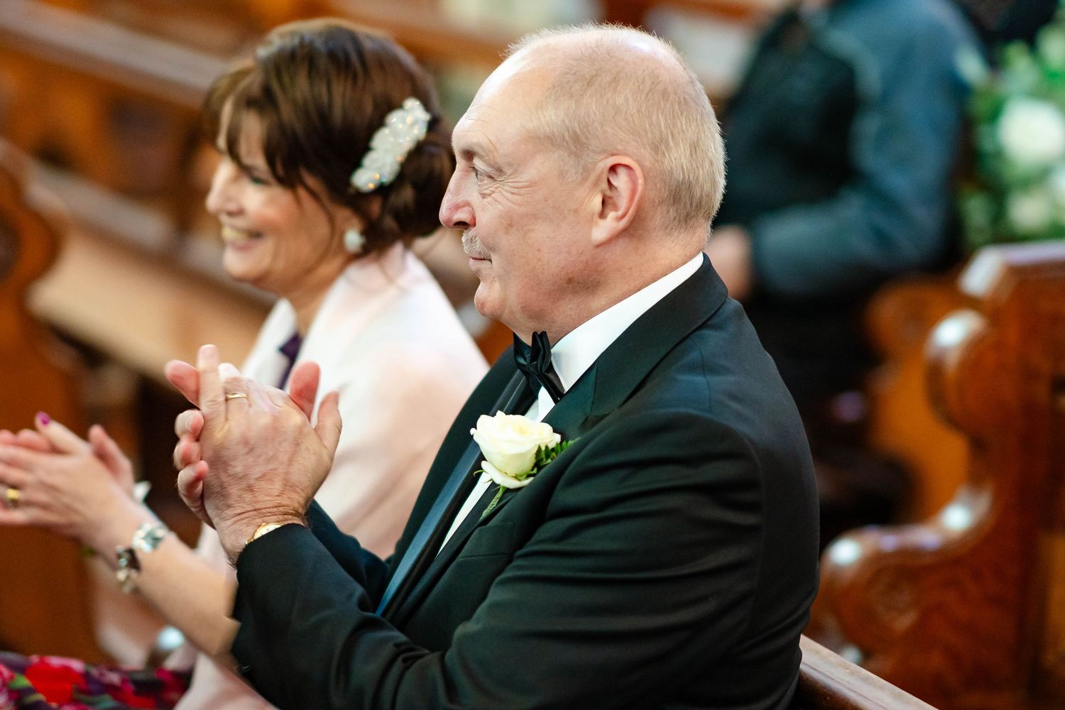 Wedding guests dressed in formal attire smile and applaud during a joyful celebration in a church setting.