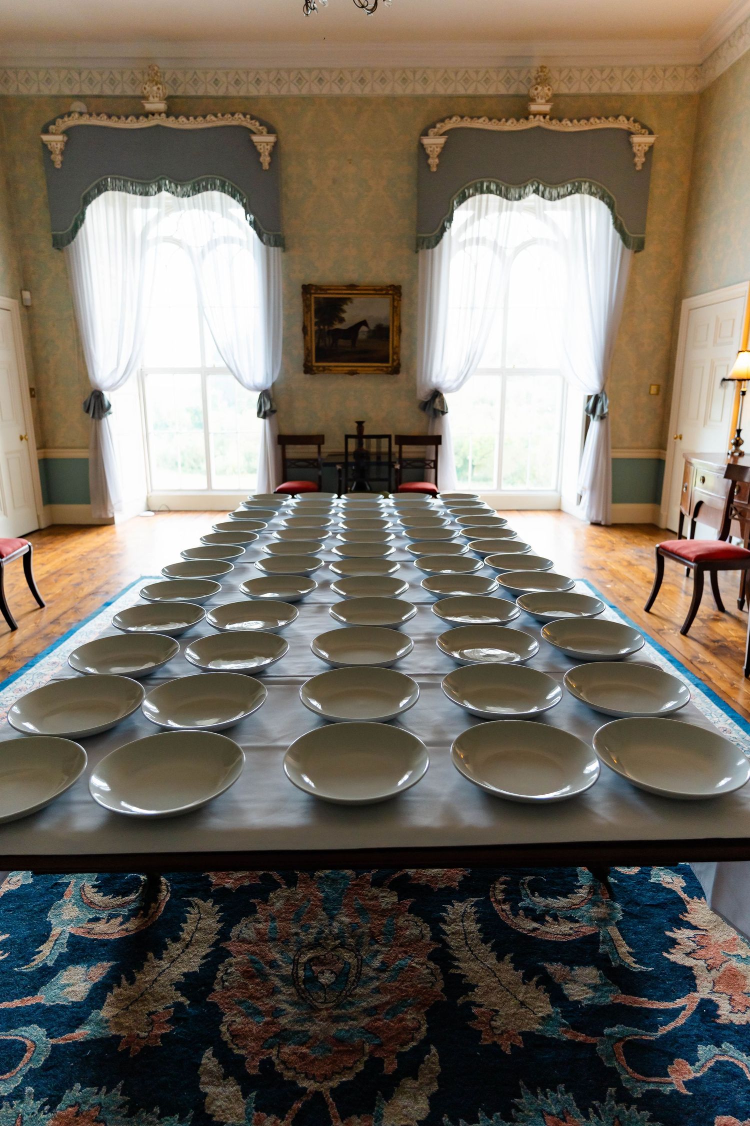 Rows of identical white ceramic bowls arranged symmetrically on an elegant dining table in a formal room with ornate decor.