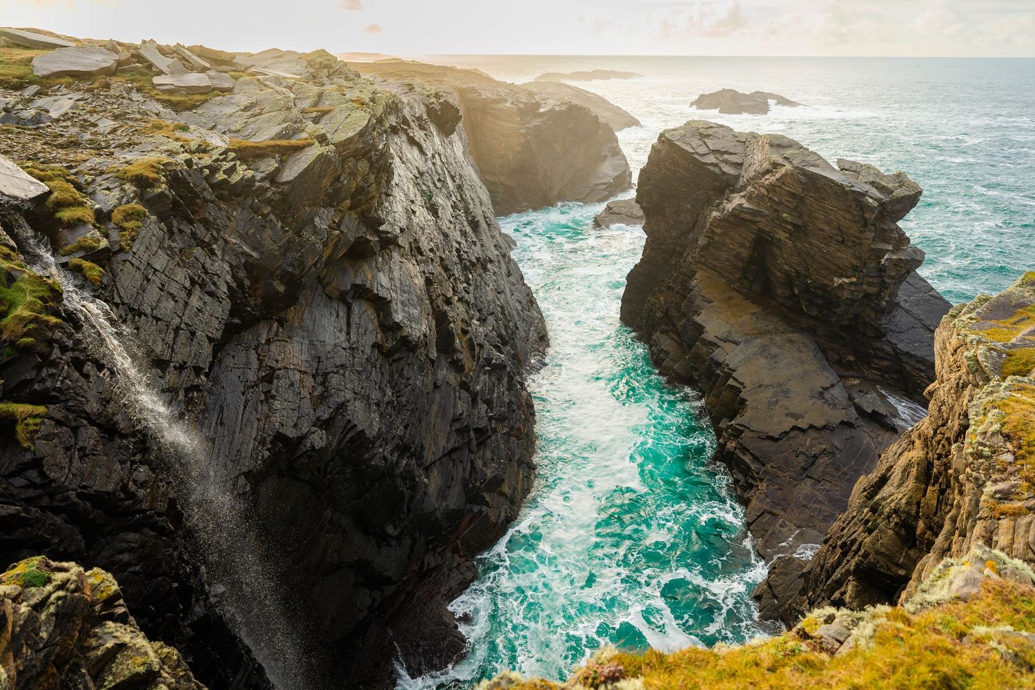 Stunning panoramic view of rocky sea cliffs with turquoise waters crashing against dark stone formations.