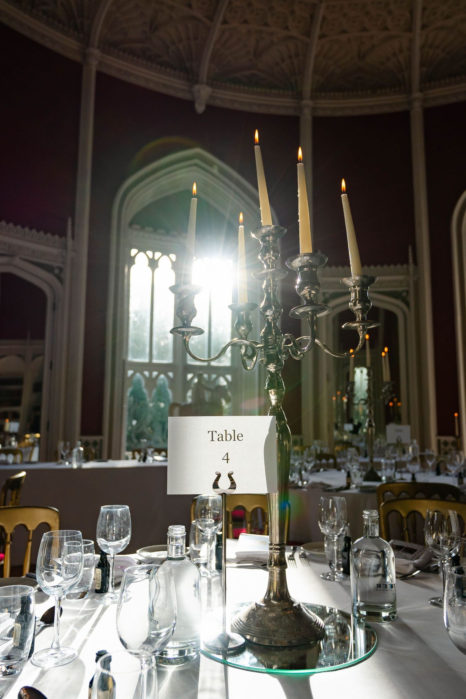 Elegant wedding reception tables set with candelabras, glassware and table numbers in a grand ballroom setting.