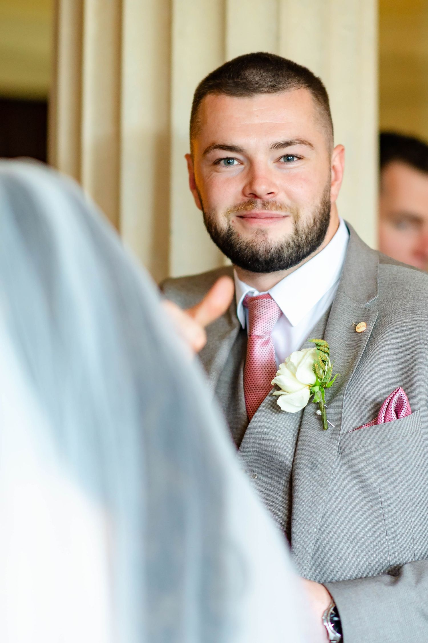 Groomsmen in matching gray suits and pink ties stand together wearing white boutonnieres at a formal wedding.