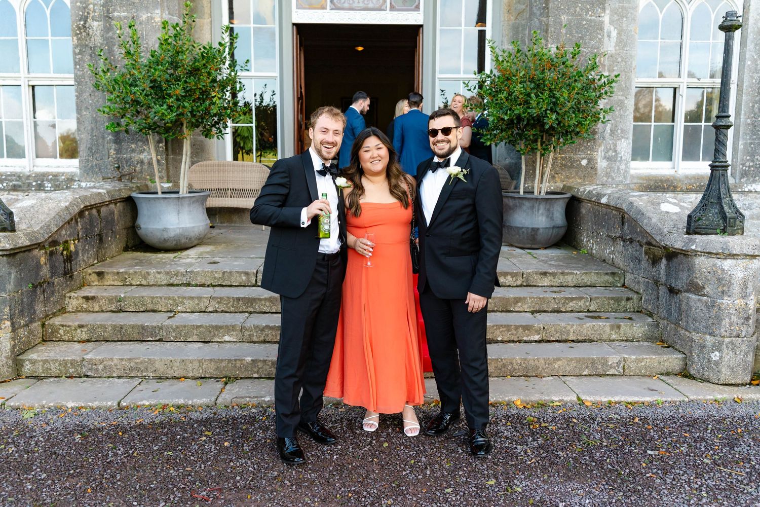 Group photo of wedding guests in formal attire standing on stone steps outside a building.