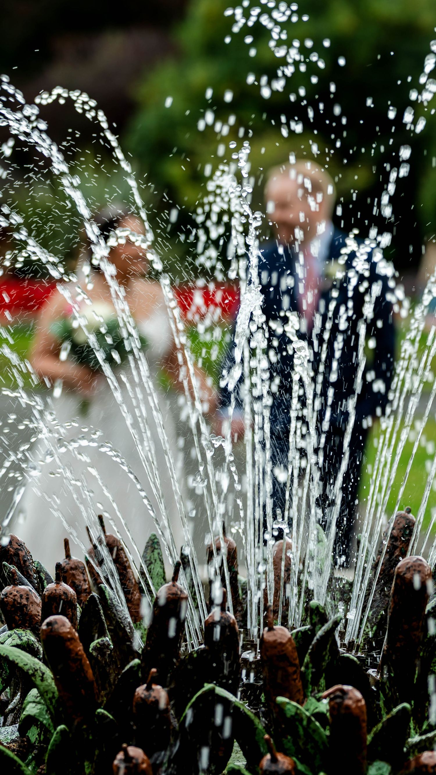 Water fountain sprays create a magical effect during an outdoor wedding photoshoot.