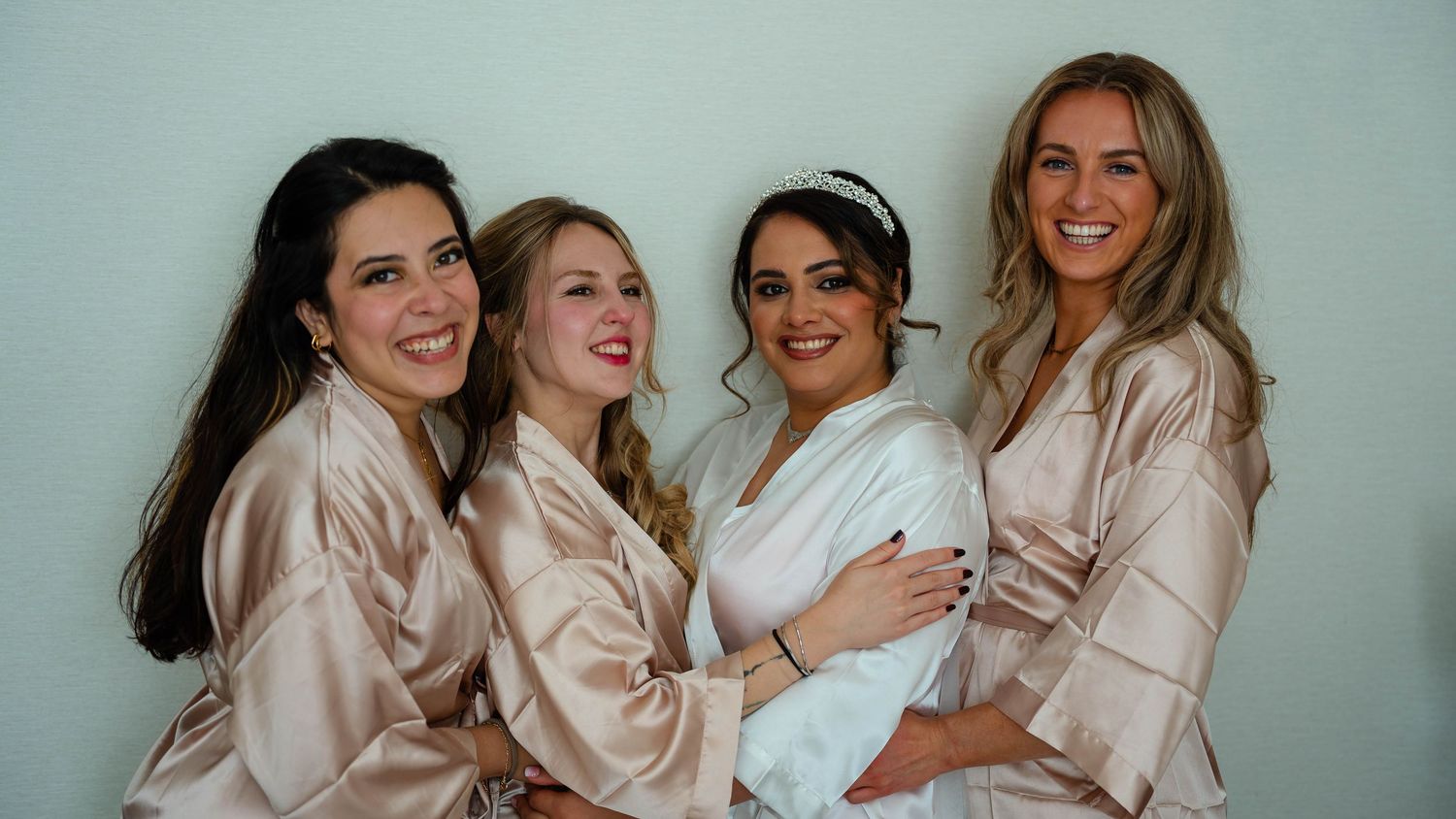 Bridesmaids in blush pink robes celebrating together in a bright room.