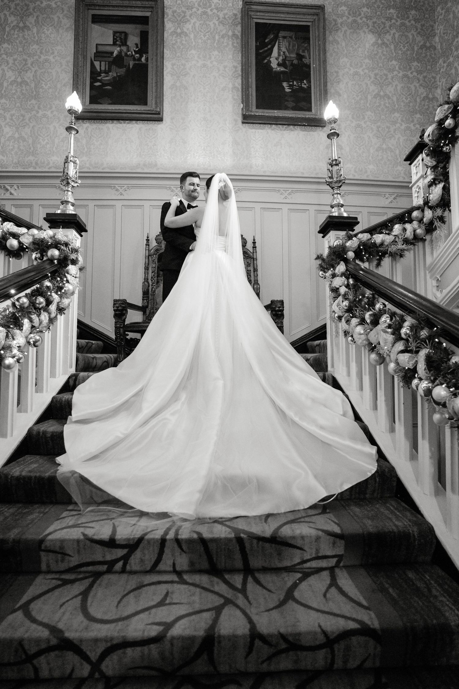 A black and white photo of a wedding dress on a grand staircase with holiday decorations.