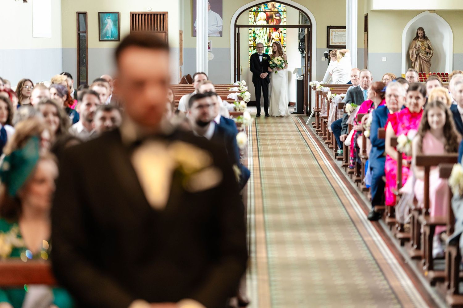 Guests seated in church pews watching a wedding ceremony procession down the center aisle.