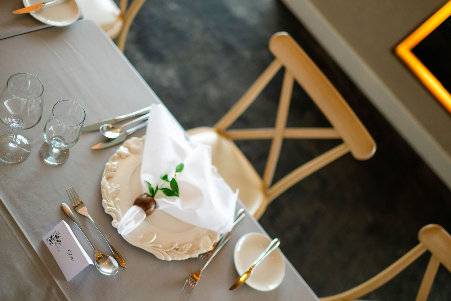 Wedding reception table setting with white napkins and cross-back chairs.