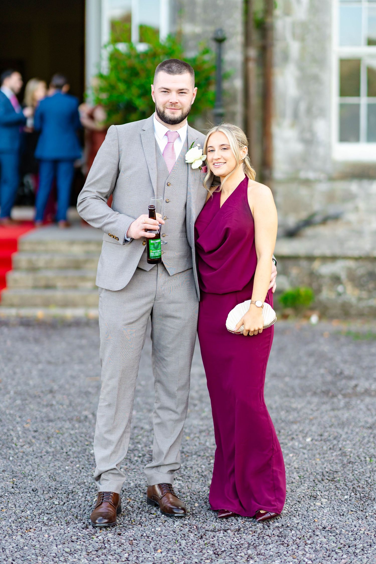 A couple at a formal event, with the man wearing a gray suit and woman in a burgundy evening gown.