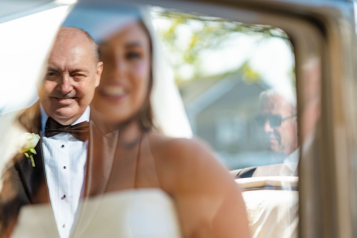 A couple in formal wedding attire seen through a car window on their special day.