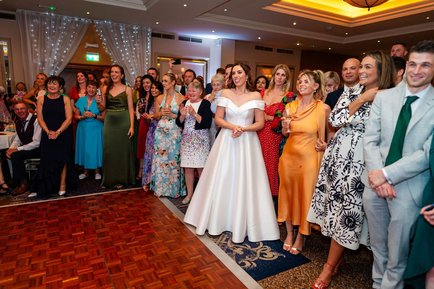 Wedding guests dancing and celebrating at indoor reception with dramatic lighting.
