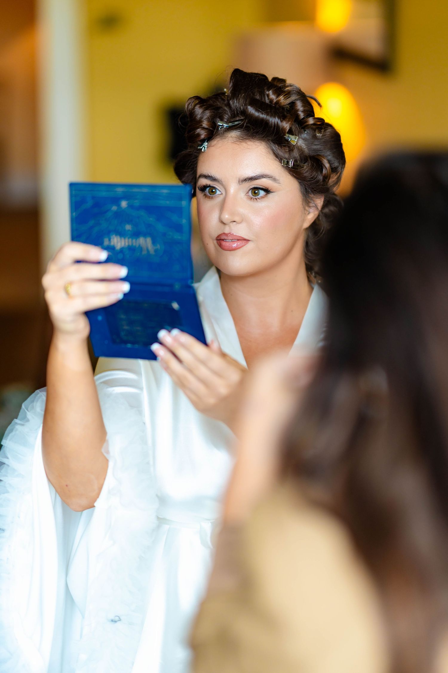 A woman in a white top examines a blue card or document in a warmly lit indoor setting.