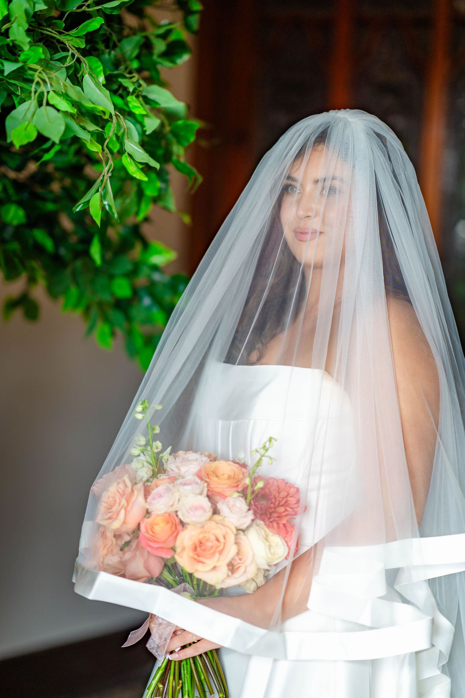 A bride in a flowing white veil holds a peach and pink rose bouquet in a series of elegant wedding portraits.