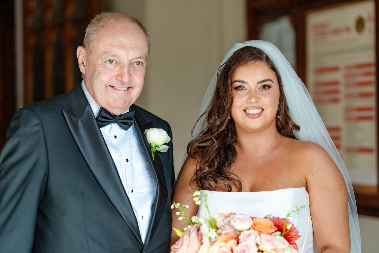 A bride in a white dress holds a colorful bouquet while standing with someone in a dark tuxedo at a wedding.