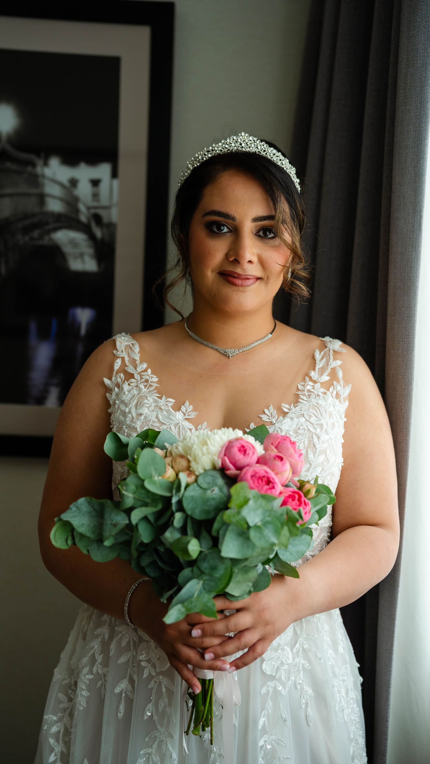 Bride in a lace wedding dress holding a bouquet with pink roses and eucalyptus.