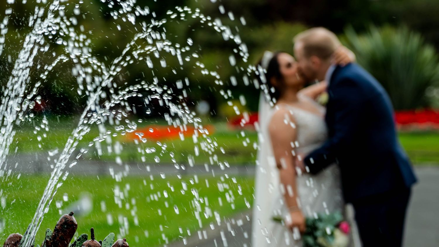 A couple embraces near a fountain with water sprays creating a romantic atmosphere.