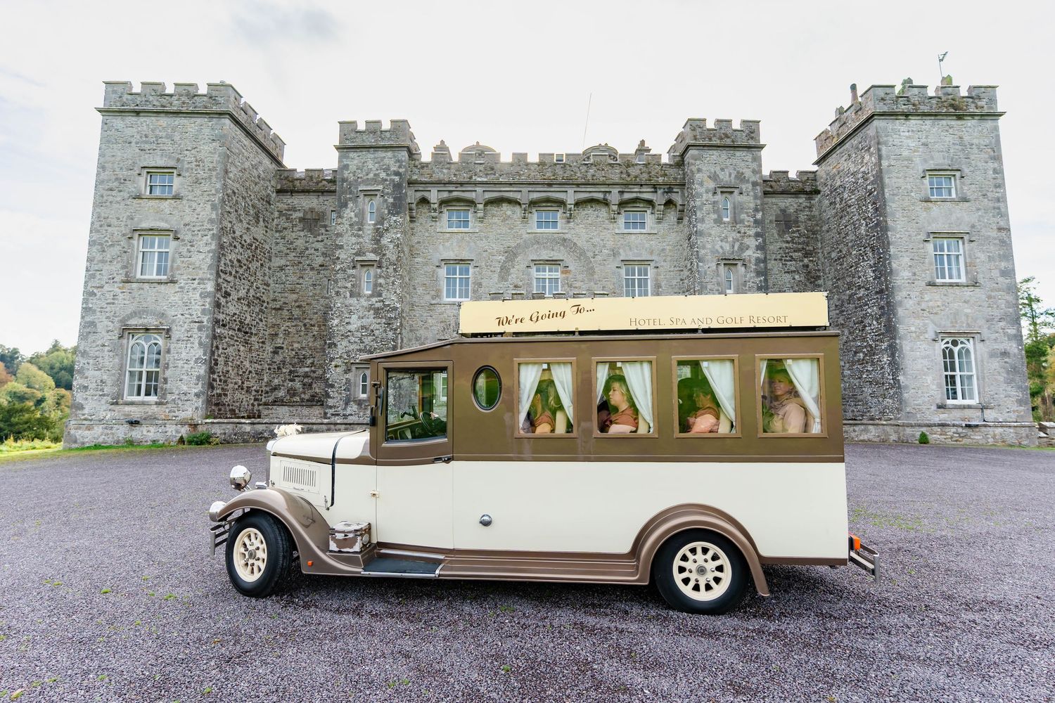 Vintage cream-colored wedding car parked in front of a majestic stone castle venue.