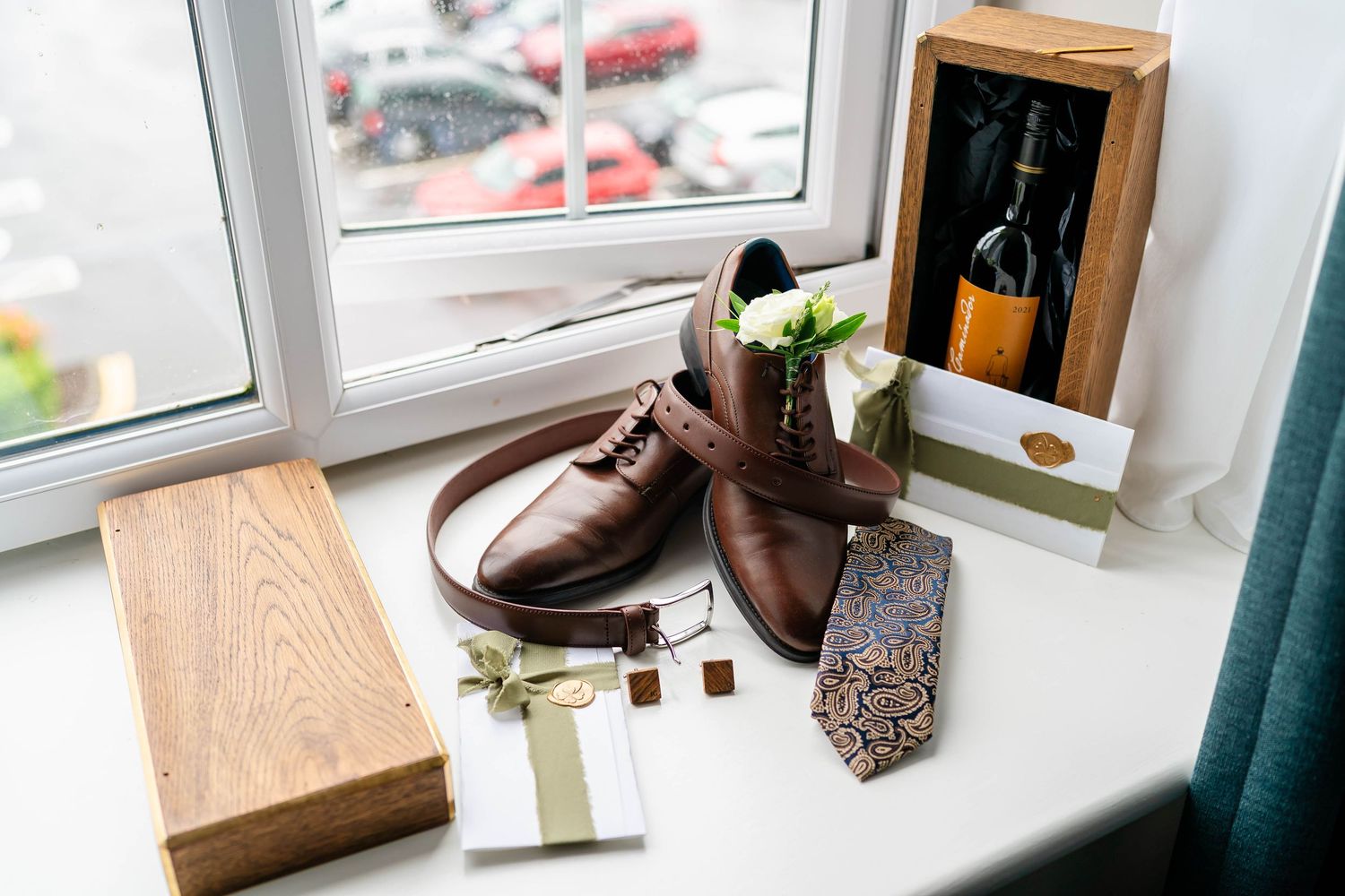 Wedding accessories including brown leather shoes and wooden box near window.