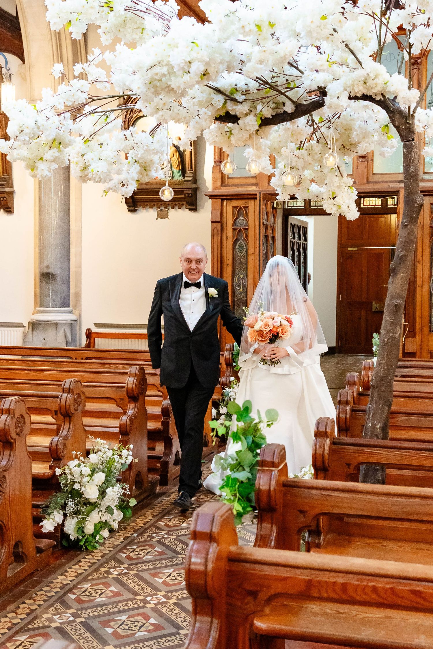 A church aisle decorated with white cherry blossom trees and floral arrangements for an elegant wedding ceremony.