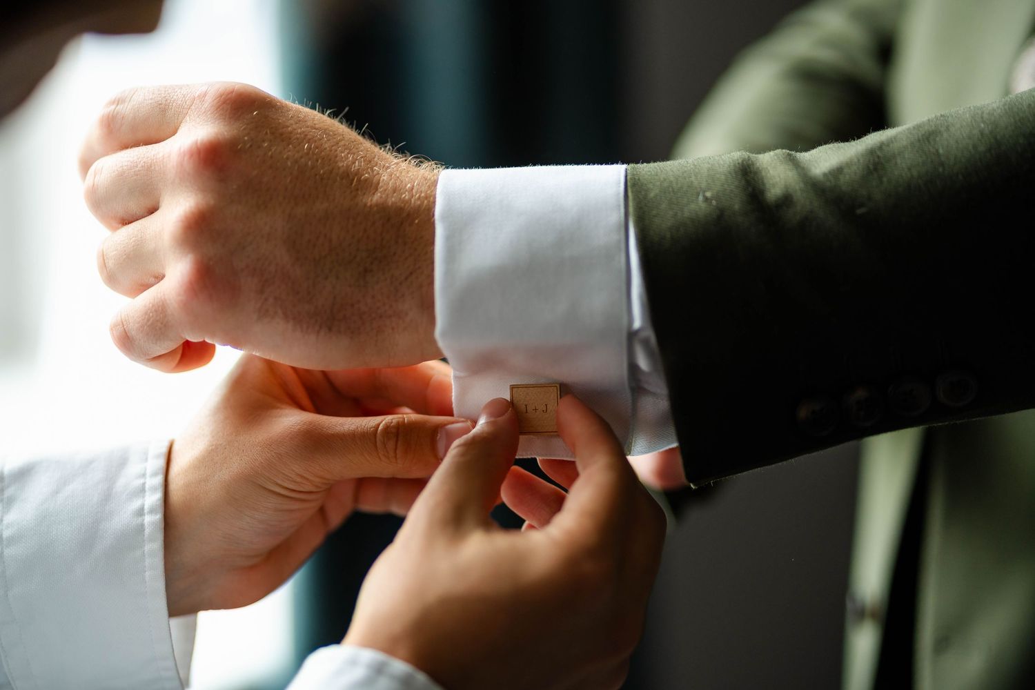Close up shot of hands helping adjust formal shirt cufflinks.