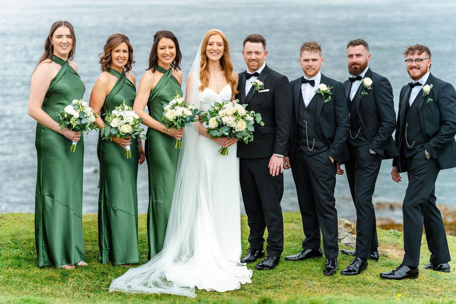 Wedding party group photos taken on green coastal cliffs with ocean views.
