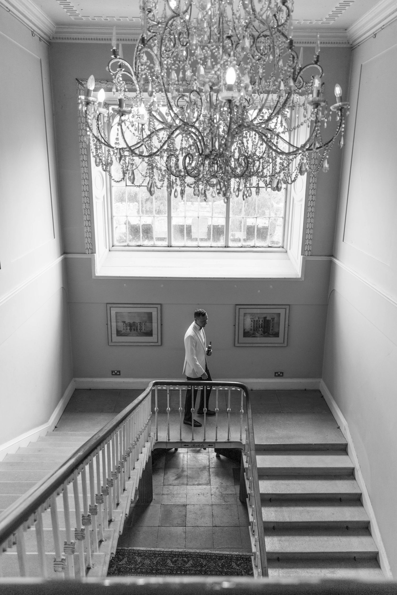 Elegant interior room with crystal chandeliers, white walls, and raised platform areas divided by white railings.