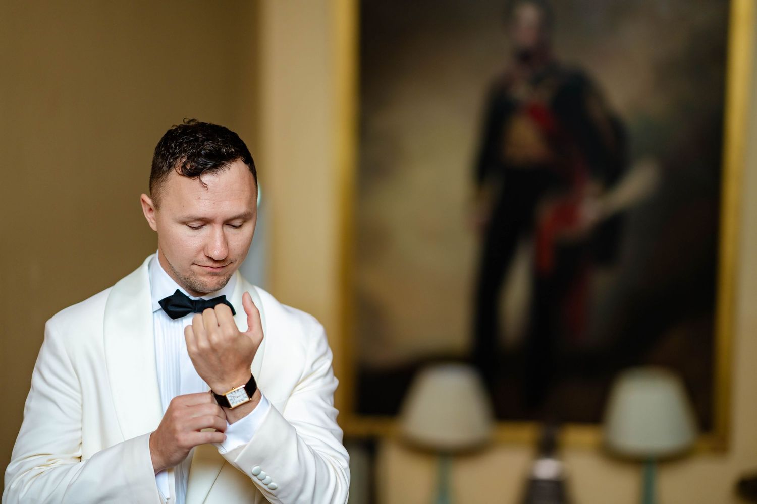 A person in a white dress shirt adjusts their tie while looking at a mirror in a formal setting.