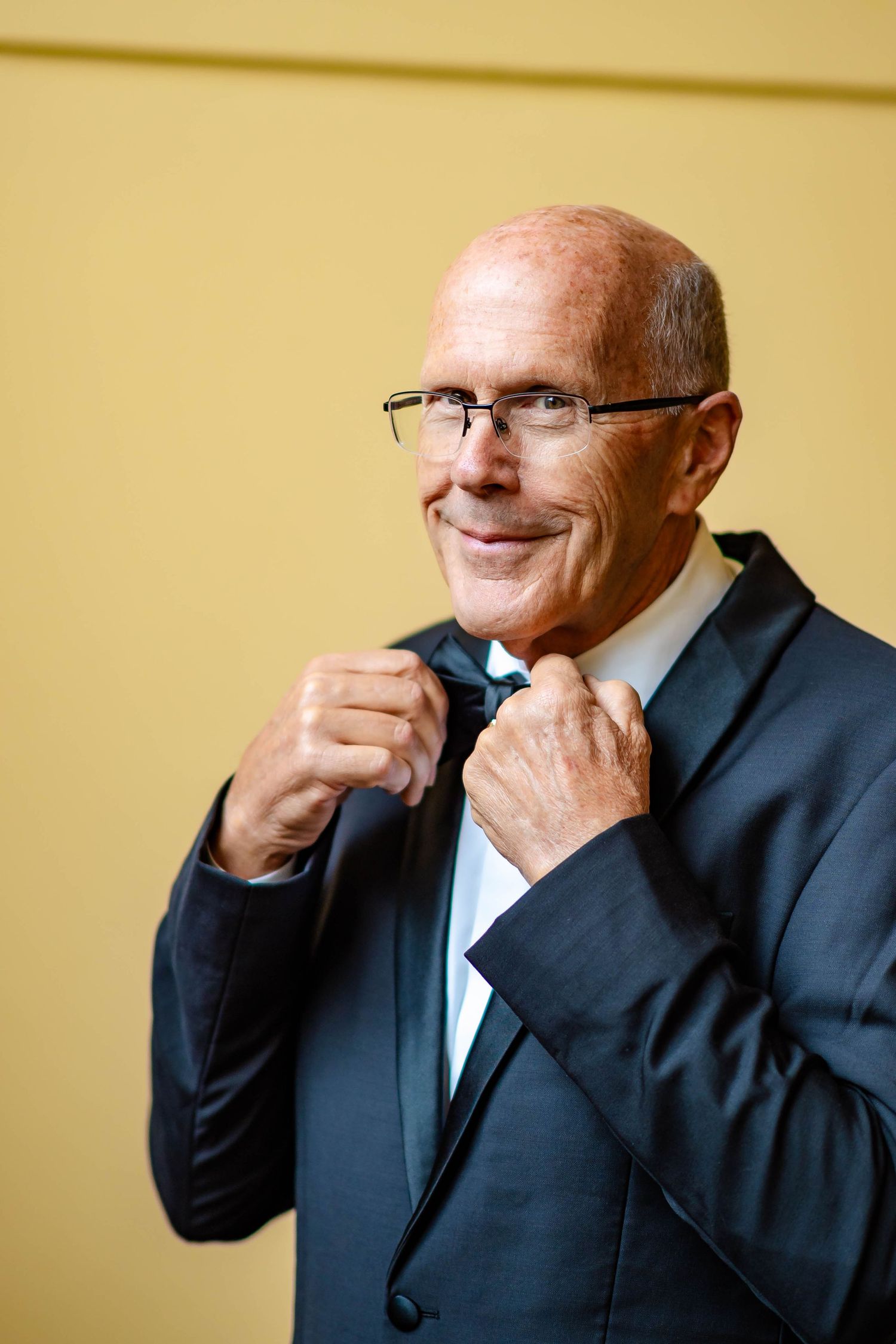 A sequence of five photos showing someone in a dark suit smiling and laughing against a beige wall.