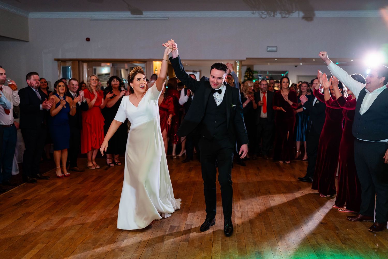 Wedding guests dancing and celebrating in a ballroom with dramatic lighting.