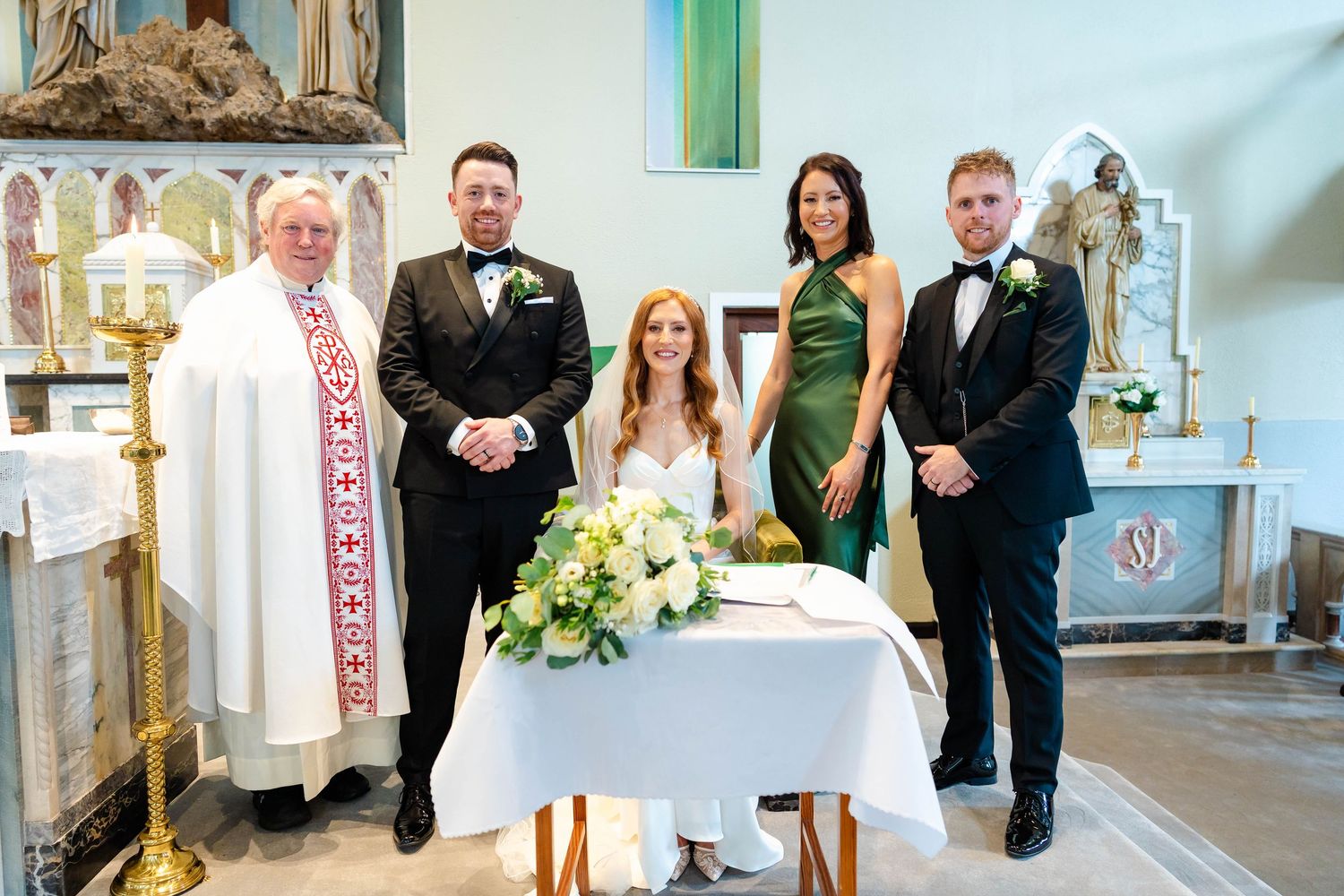 Wedding party members gathered near altar in traditional church setting.