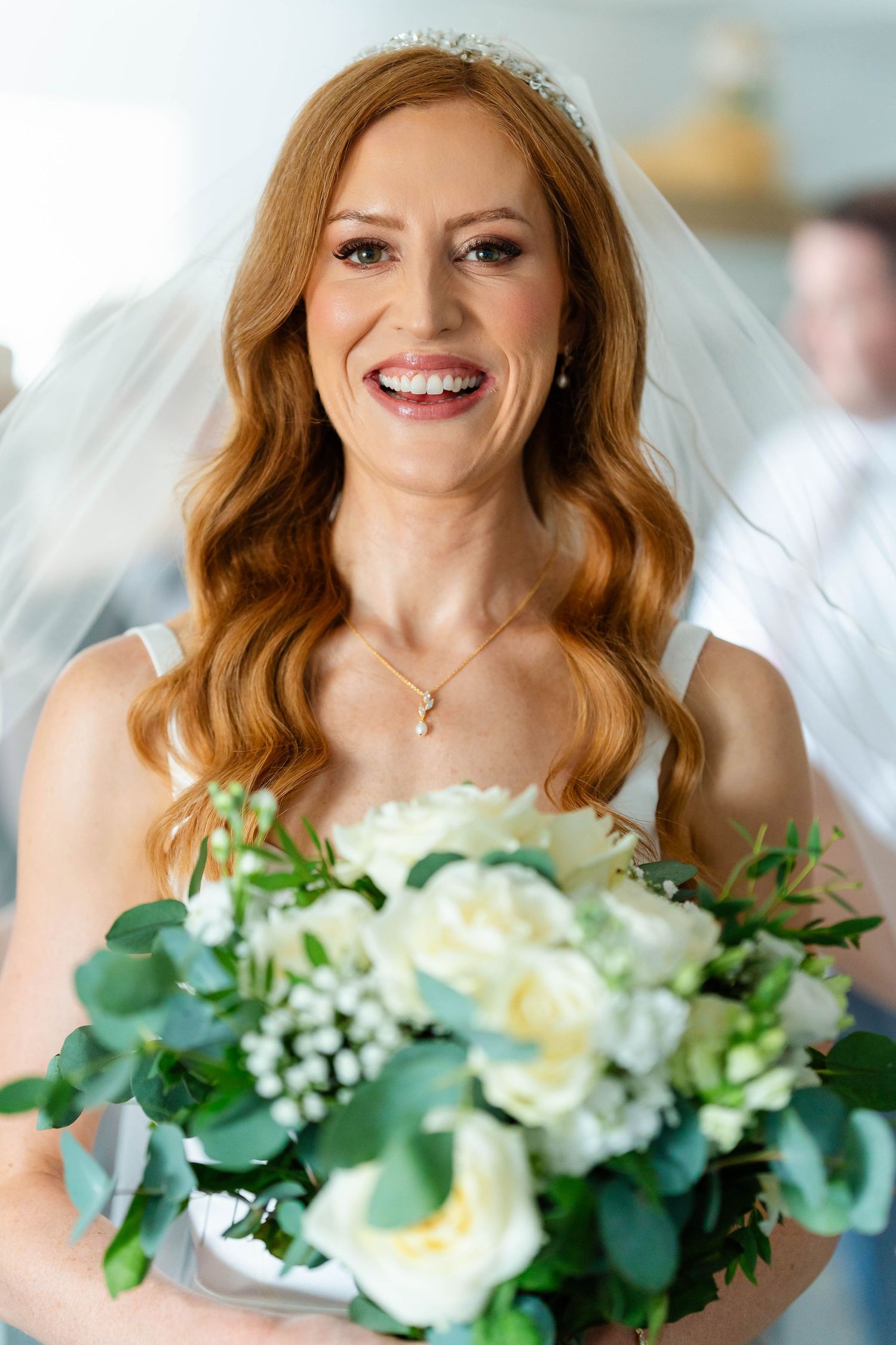 Beautiful bridal bouquet of white roses and eucalyptus held against white wedding dress.