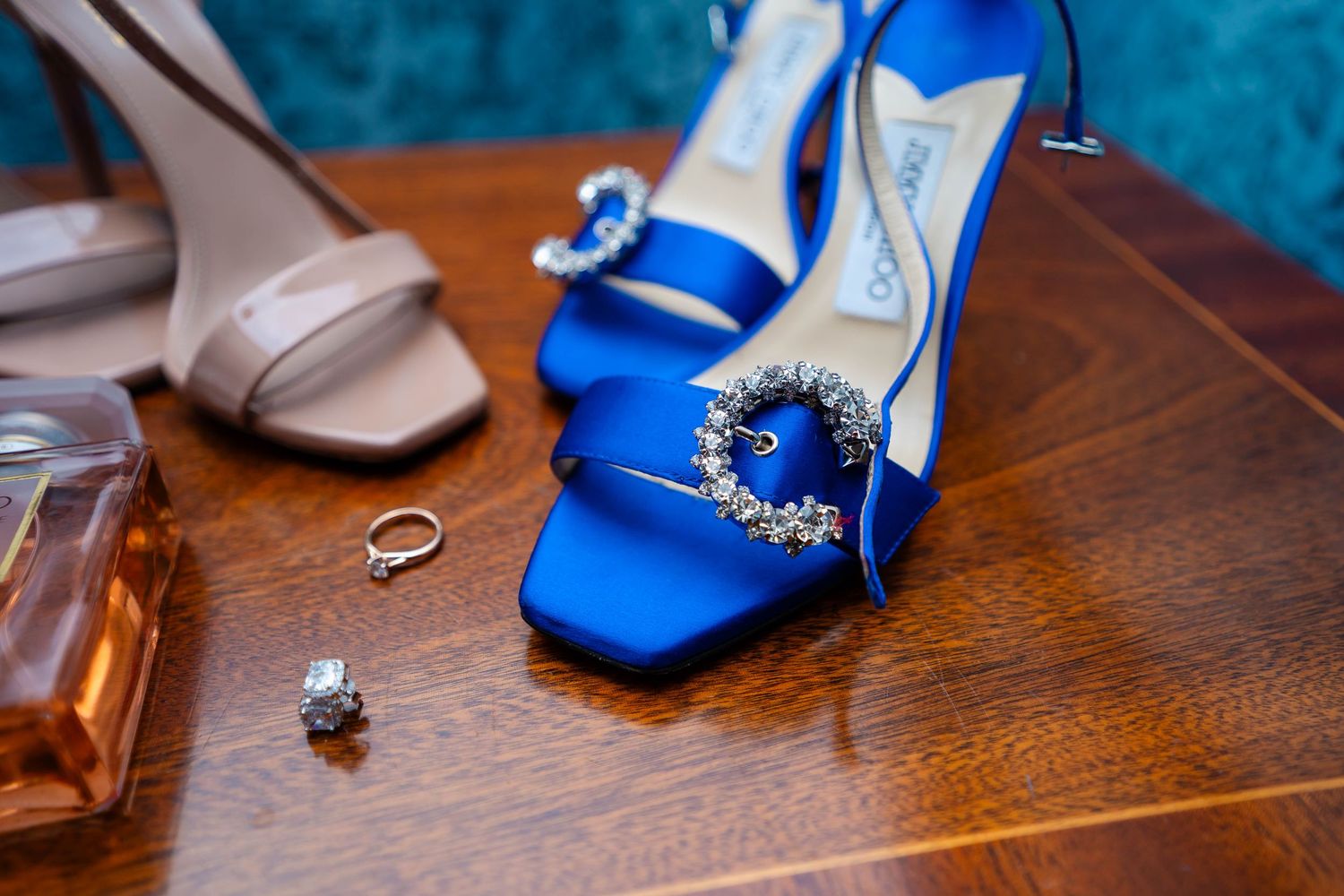Wedding accessories including blue heels and jewelry arranged on a wooden surface.