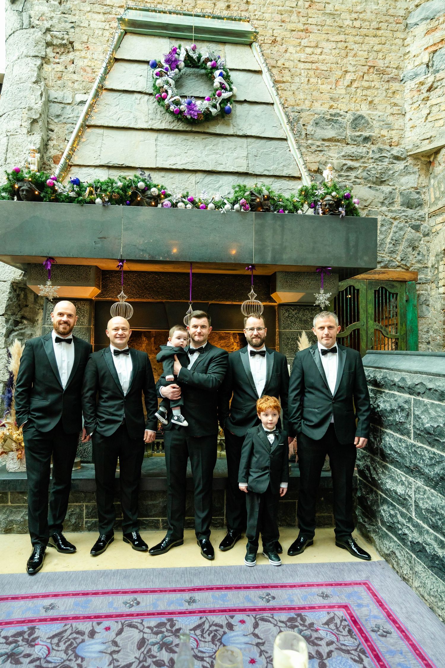 Group in formal attire sitting on stone ledge with decorative carpet below.