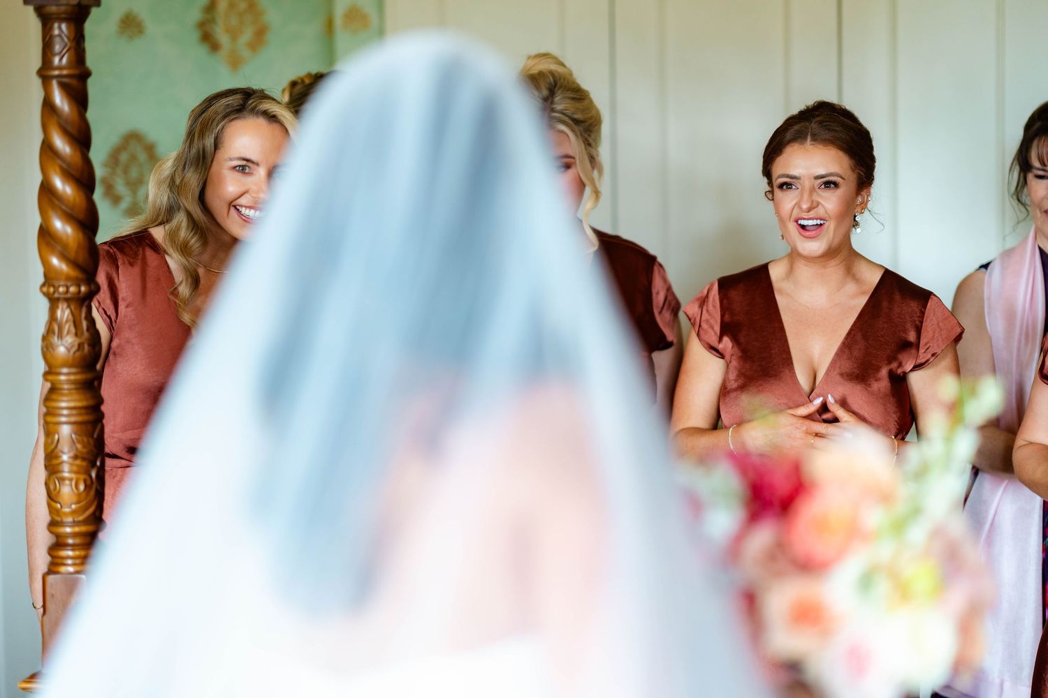 Bridesmaids in matching mauve gowns react with joy during wedding first look moment.