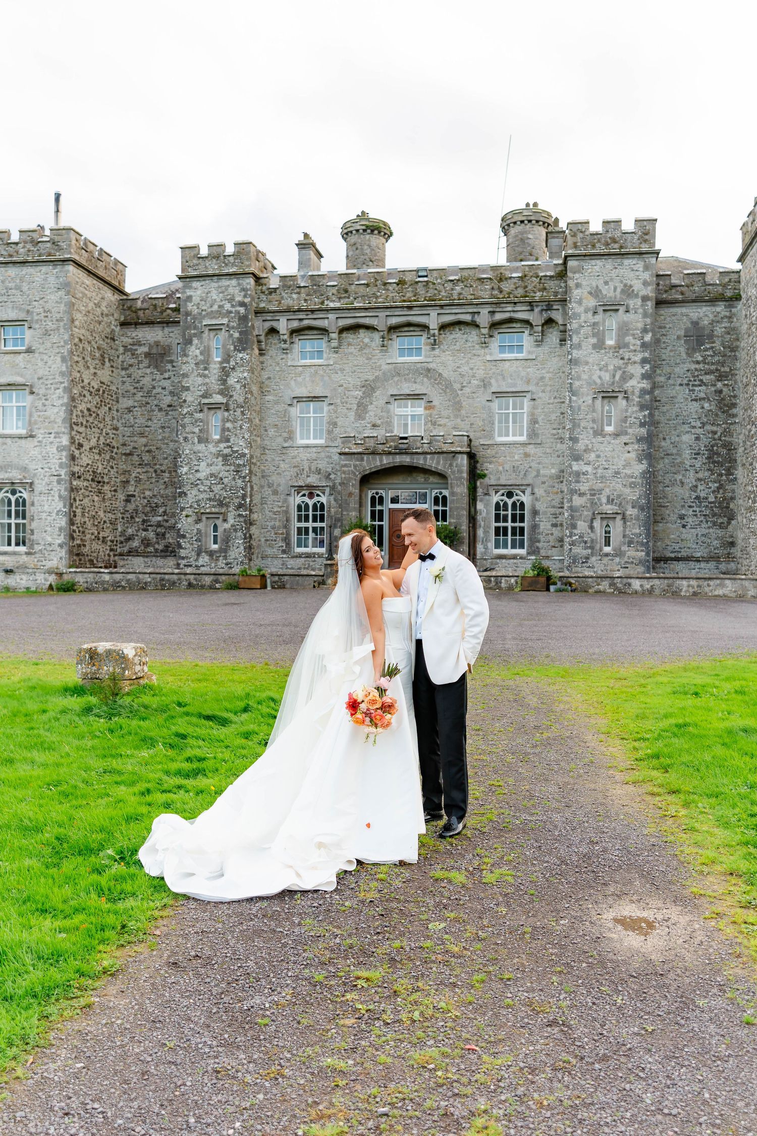 A wedding couple poses for romantic photos outside a historic stone castle with grey walls and windows.