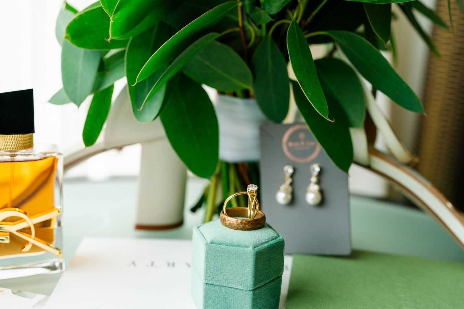 Wedding details including perfume bottles, greenery, and delicate decor arranged on a white surface.