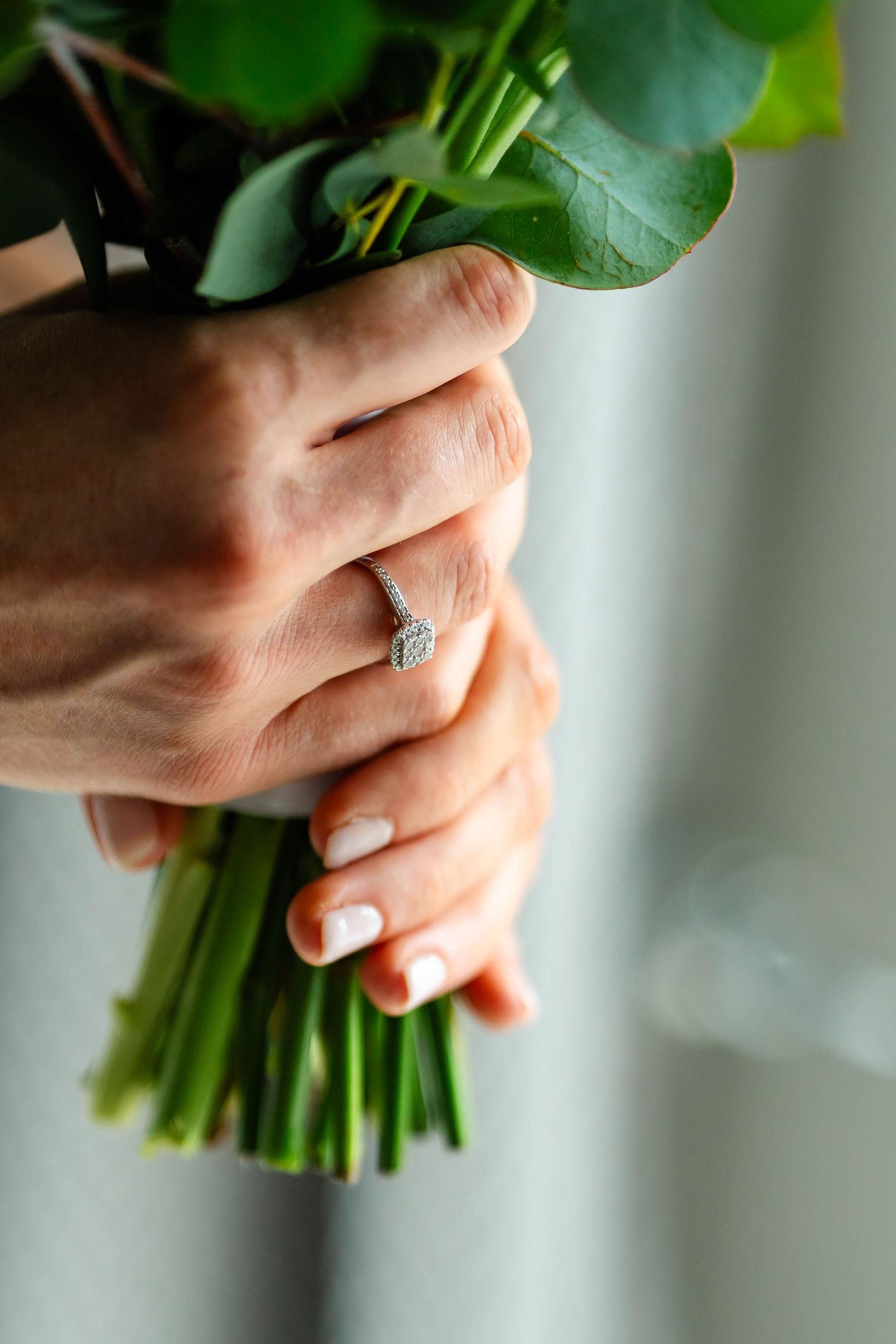 Close-up of hands holding a fresh green bouquet with white flowers and eucalyptus leaves.
