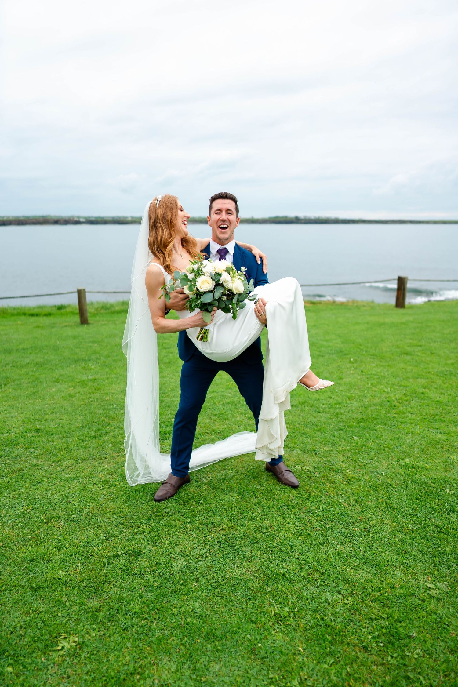 A playful wedding photoshoot on green grass with a waterfront backdrop.