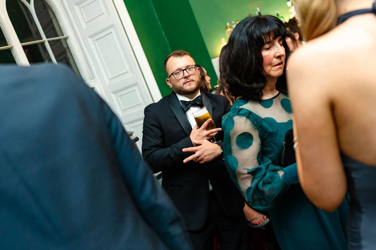 People mingling at an evening party with blue and green lighting in an elegant interior space.