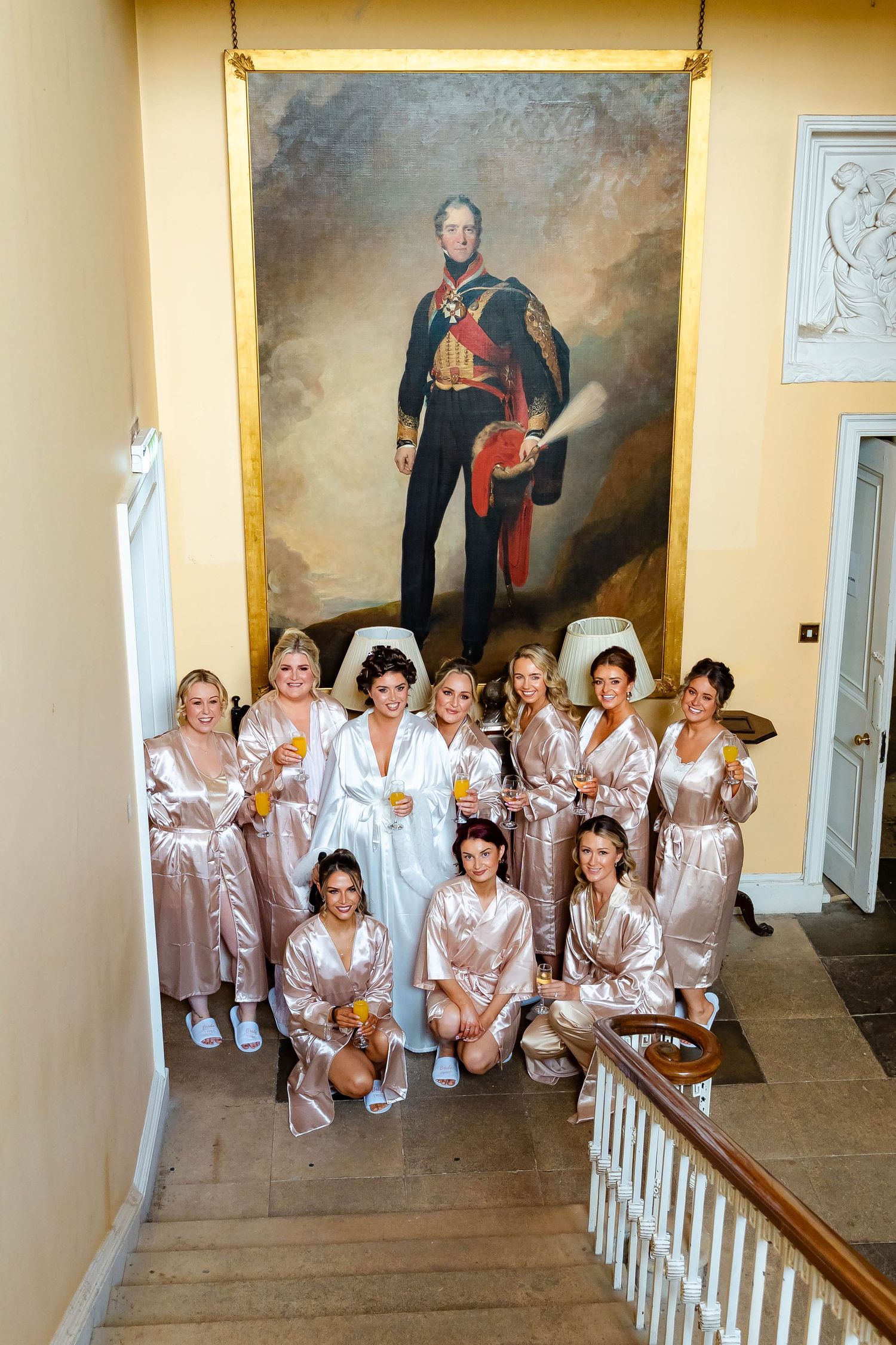 Wedding party in matching silk robes poses together on an elegant staircase.