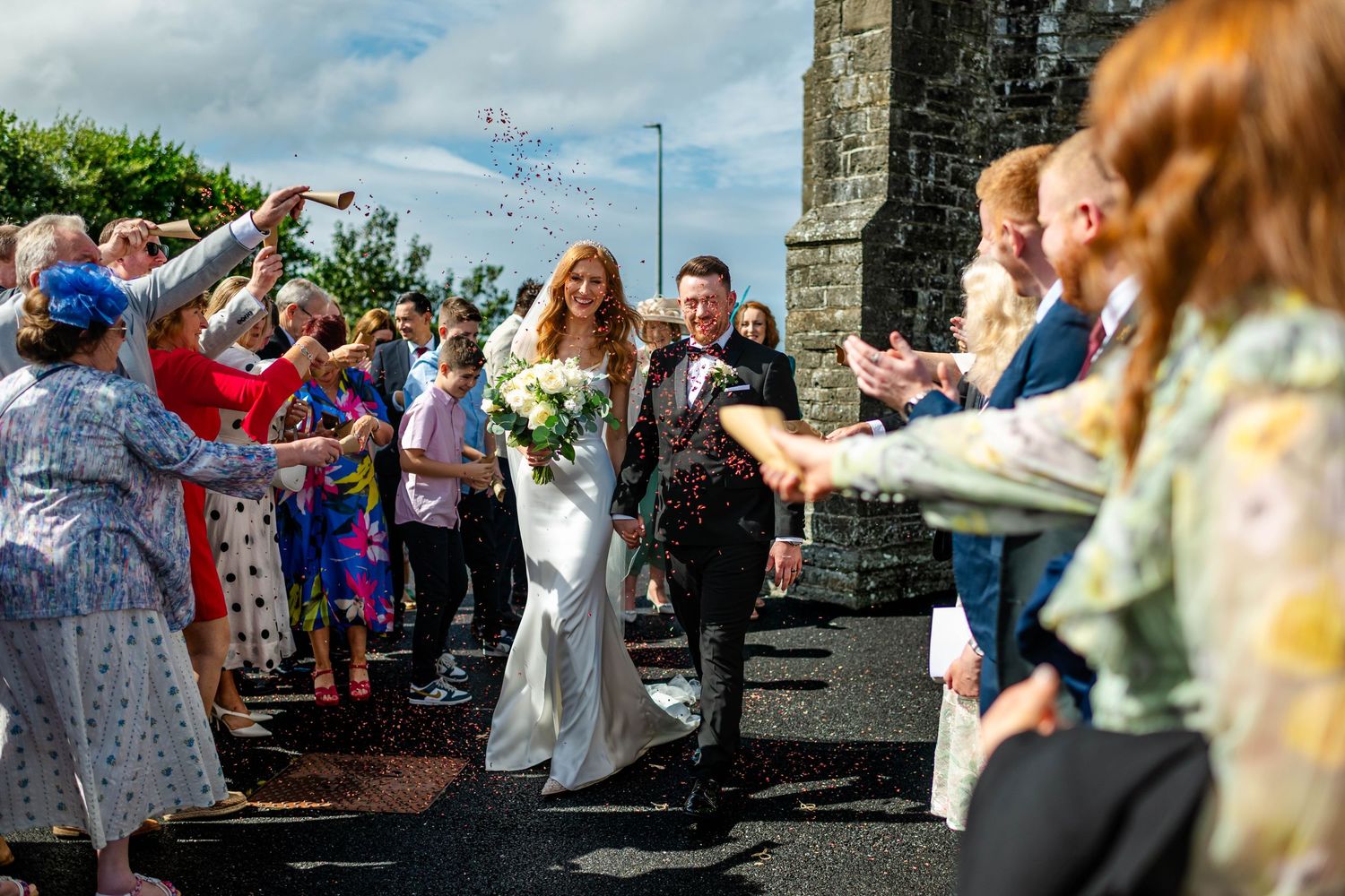 Celebratory moment with wedding guests tossing confetti in front of stone architecture.