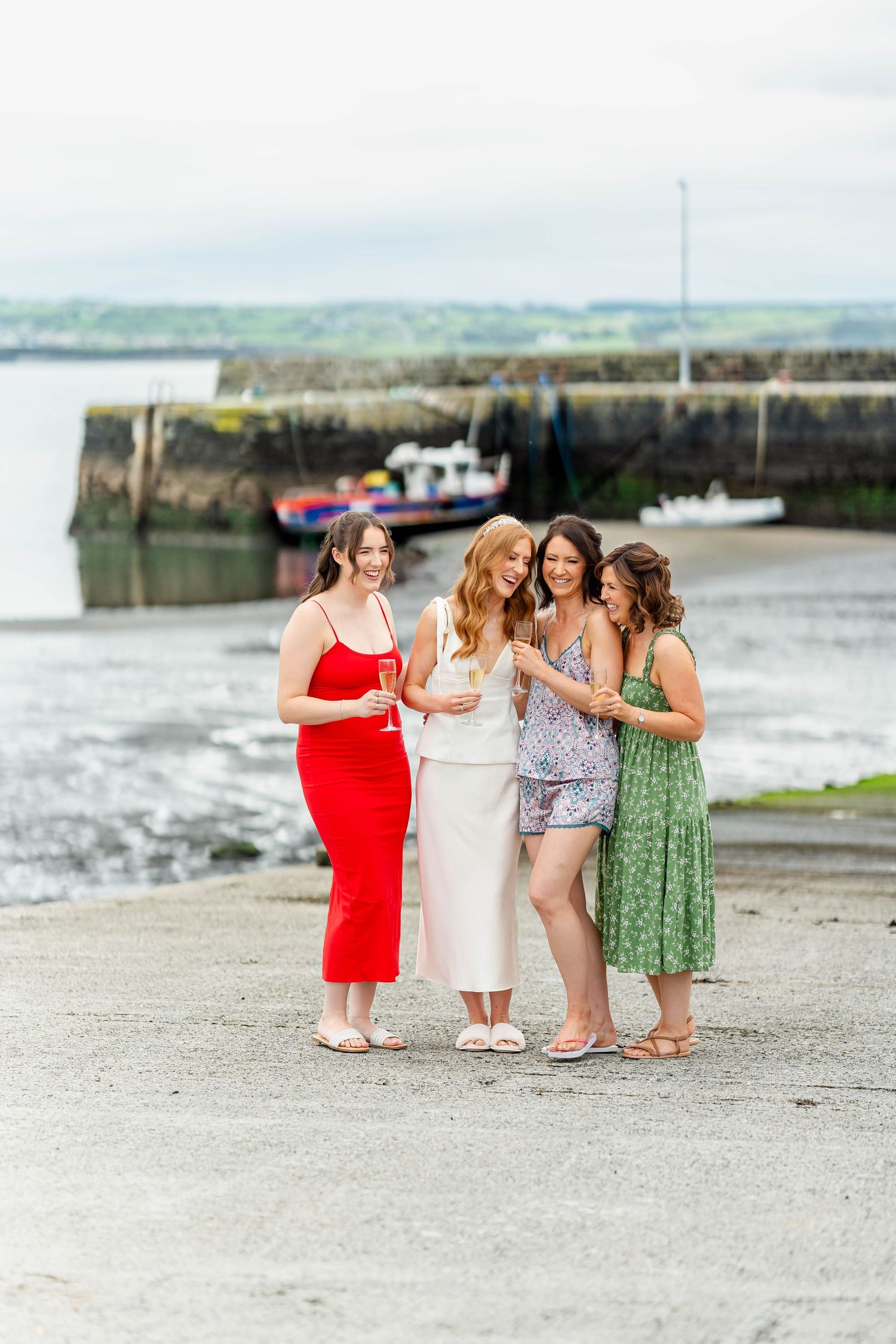 Women in elegant dresses gather for photos on a coastal pathway.