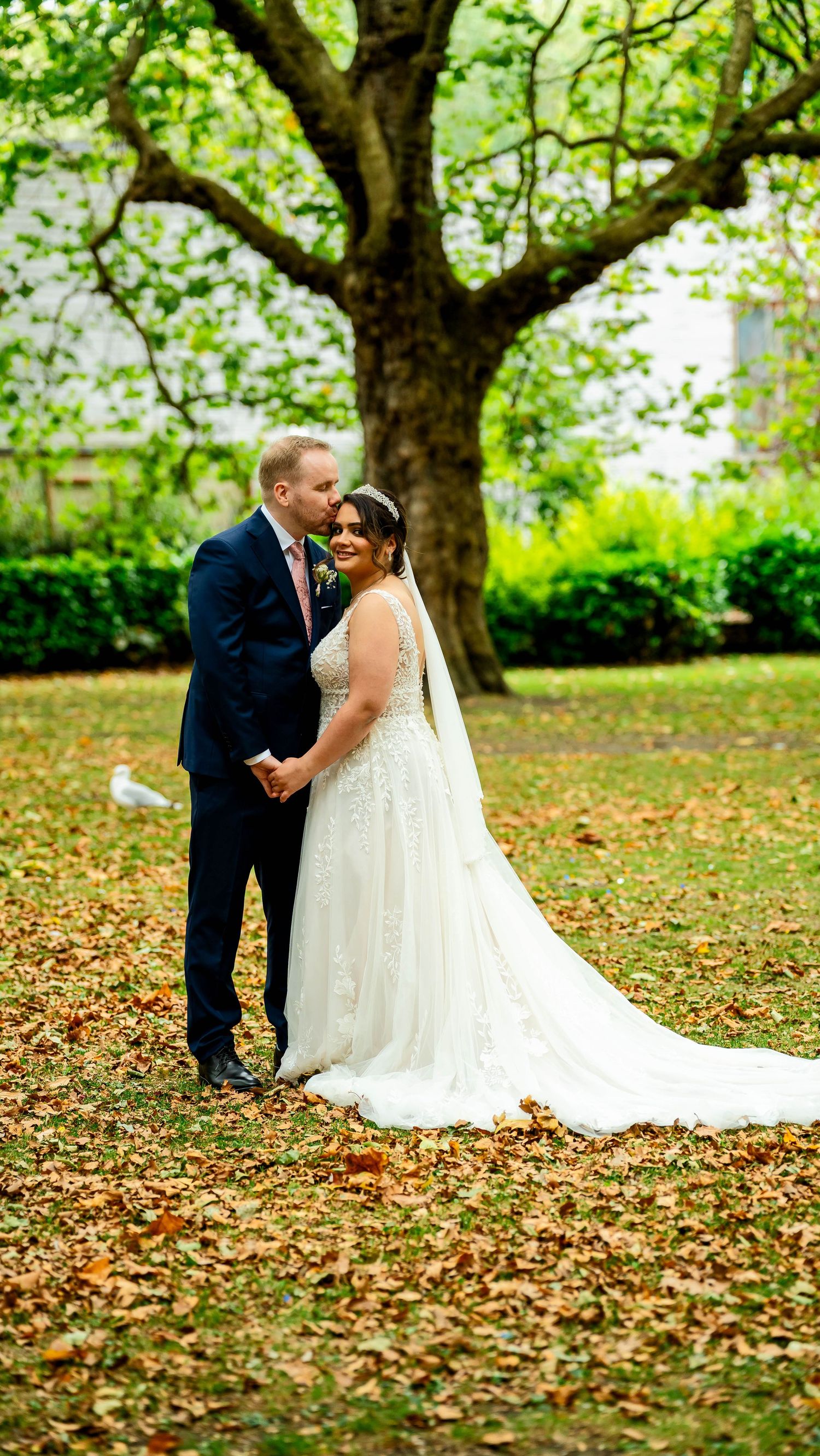 A couple shares intimate wedding photos among fallen autumn leaves in a park.